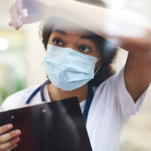 Young tired overworked african american medical worker in protective face mask looking out of window